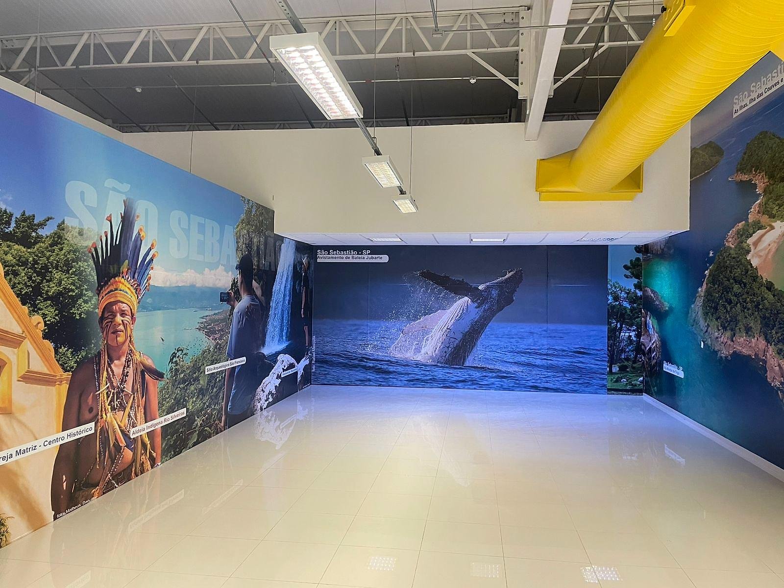 Painéis de parede com paisagens de São Sebastião, uma baleia e um indígena, no Aeroporto Mall